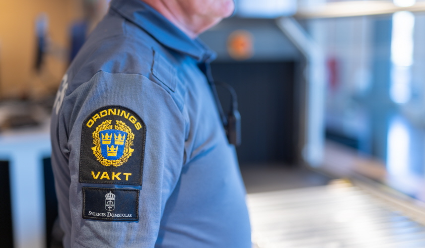 Närbild på en ordningsvakts uniform, emblem och telefon syns