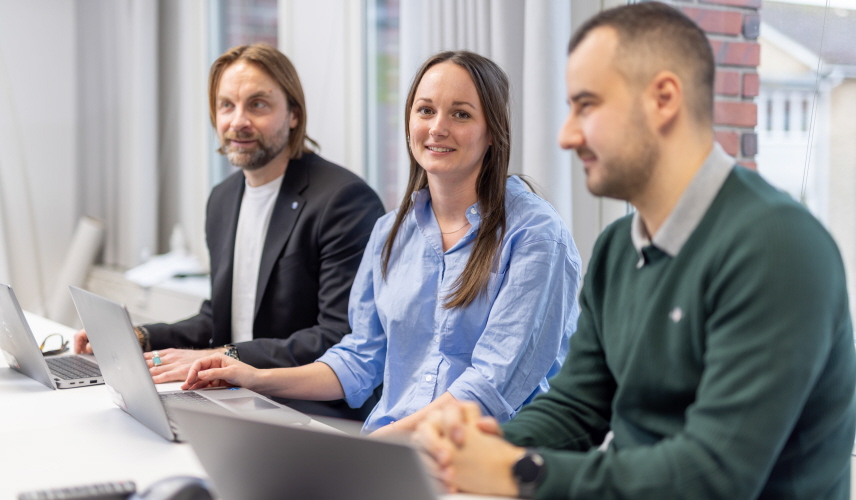 Två män och en kvinna sitter vid bord med laptops.