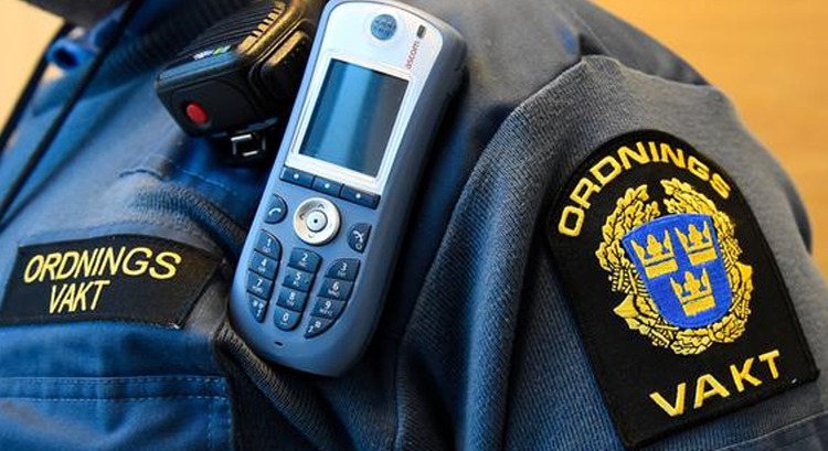 Närbild på en ordningsvakts uniform, emblem och telefon syns