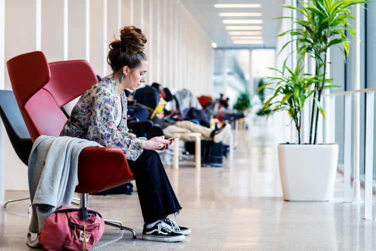 Ung kvinna i fåtölj i offentlig lokal, håller en mobiltelefon.