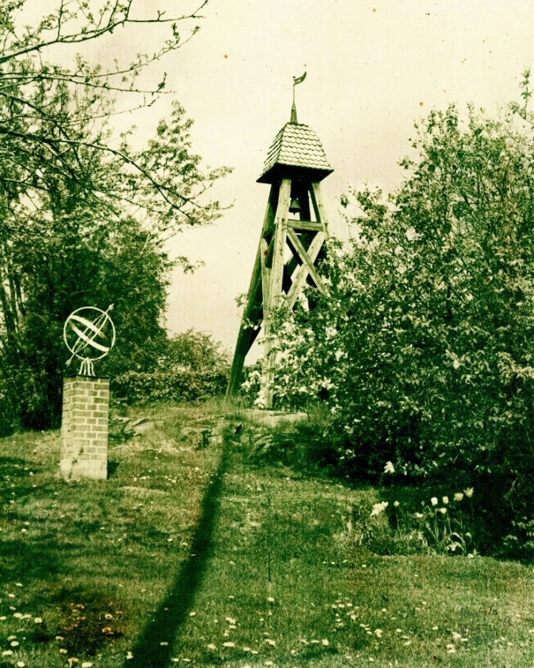 Fotografi av Östra Värends tingsklocka på kulle med solur i järn och gröna buskar i förgrunden 1967