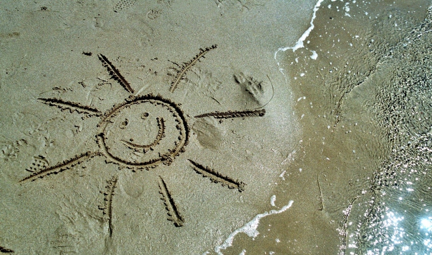 En glad sol ritad i sanden på en strand