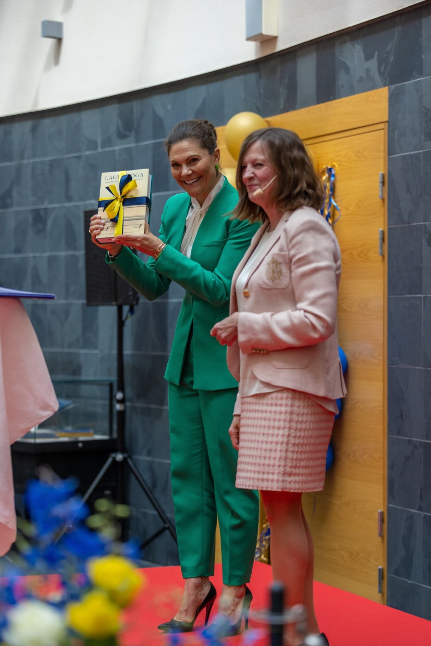 Kronprinsessan håller upp en bok med blågul rosett.