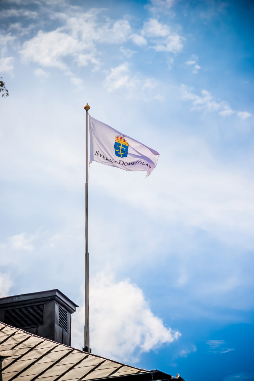 Sveriges Domstolars flagga på en flaggstång mot blå himmel med lätta moln