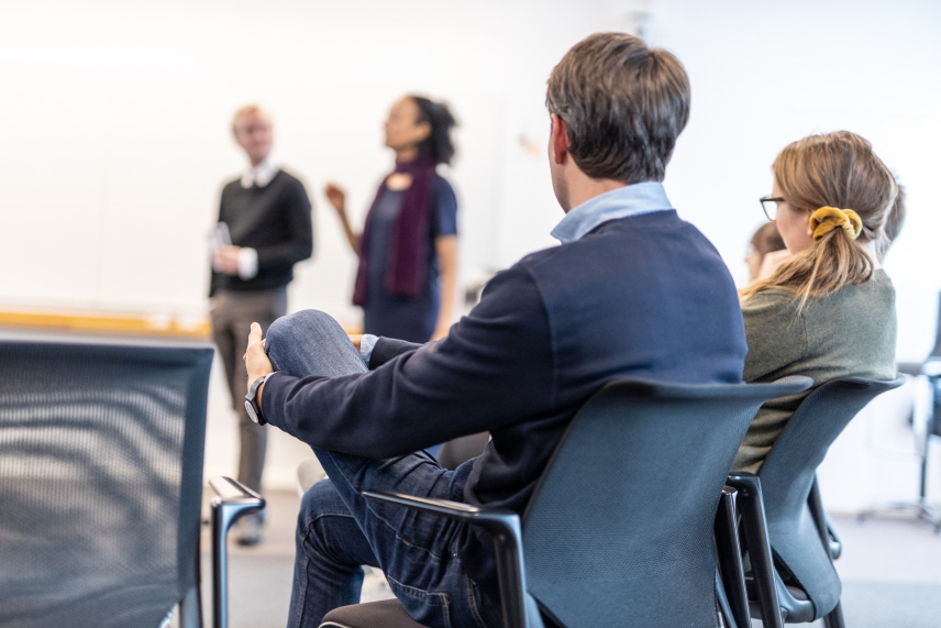 Två personer sitter och lyssnar till två föredragshållare. 