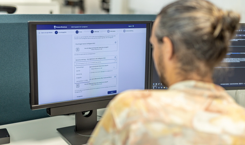 En handläggare på myndighet använder en e-tjänst som visas på en datorskärm. 