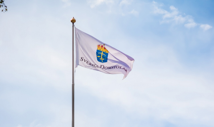 Sveriges Domstolars flagga på en flaggstång mot blå himmel med lätta moln