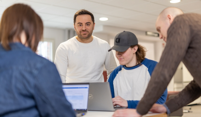 Tre män och en kvinna tittar in i laptops, diskuterar.